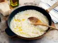 Krämig risotto i panna, med parmesan, olivolja och en träsked. Perfekt för ett enkelt risotto recept.