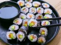 En tallrik med hemgjord sushi, perfekt för ett enkelt sushi recept. Lax och avokado rullade i ris och nori, med en skål sojasås.