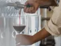Rött vin hälls upp i ett glas från en stor tank. En hand vrider på kranen, kanske för att kontrollera tillsatser i vin.