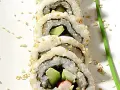 En närbild på en california roll med sesamfrön och en grön garnityr.