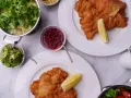 Två krispiga schnitzlar med citronklyfta, serverade med potatissallad, lingon, gurksallad och en krämig sås. Ett perfekt schnitzel recept för en festmåltid.