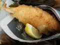 Krispigt friterad fisk med citronklyfta, inslagen i tidningspapper. En klassisk fish and chips-upplevelse.