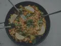 En stor panna med jollof rice, räkor, citronklyftor och färsk persilja. Tre bestick ligger redo att avnjutas.