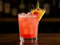 En rosa Singapore Sling med is, garnerad med en körsbär och ananasskiva.