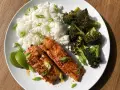 Två saftiga filéer av asiatisk lax serveras med fluffigt ris, rostad broccoli och limeklyftor.