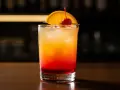 En klassisk tequila sunrise med lager av rött och orange, garnerad med apelsinskiva och körsbär.
