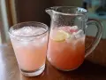 Ett glas och en karaff fyllda med rosa rabarbersaft med is och citronskivor. Perfekt för ett rabarbersaft recept.