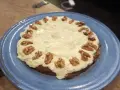 En saftig glutenfri morotskaka med krämig frosting och valnötter på en blå tallrik.