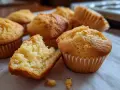 Nybakade, gyllene glutenfria muffins ligger uppradade. En är uppbruten och visar en fluffig insida. Perfekt för fikat!