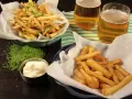Två skålar med krispiga pommes frites, en med grön kryddning, bredvid två glas öl och en skål majonnäs.
