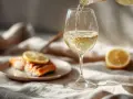 Ett glas vitt vin hälls upp, perfekt vin till lax. En citronskiva vilar på den saftiga fisken.