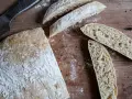En hel och skivad ciabatta på en träskärbräda, redo för ett gott ciabatta recept. Mjöl strött över.