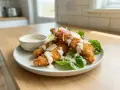 Krispiga bitar av panerad kyckling serveras med sallad, parmesan och en krämig dressing. En härlig rätt som passar perfekt till lunch eller middag.