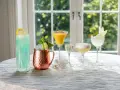 Fem olika vodka drinkar, från en blå long drink till en gyllene passionfruktscocktail och en vit äppeldryck, står uppradade på ett dukat bord.