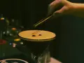 En hand lägger kaffebönor på en krämig espresso martini.
