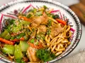 En skål med kycklingwok med nudlar, grönsaker och sesamfrön. En härlig och färgstark måltid.