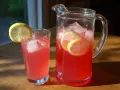 En karaff och ett glas med rosa lemonad, is och citronskivor. Perfekt för ett enkelt lemonad recept.