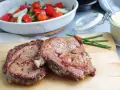 Två saftiga entrecôte-biffar på skärbräda, redo för ett utsökt entrecote recept. Grönsaker i bakgrunden.