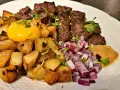 En tallrik med biff Rydberg: tärnad biff, stekt potatis, rå äggula, hackad rödlök och en klick sås. Perfekt vin till biff rydberg!