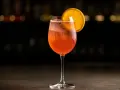 Ett glas med bubblig, orange drink, troligen en cava aperol, med en apelsinskiva som garnering.