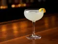 En elegant drink, en "white lady", står på en träbar. Den är garnerad med en citronskal.