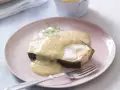 En bit fisk täckt med krämig beurre blanc-sås, garnerad med dill, serveras på en ljusrosa tallrik med en gaffel.
