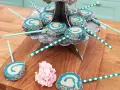 Blå och vita cake pops med strössel på ett silverfärgat fat. Vissa ligger på ett träunderlag med rosa blommor.