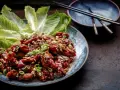 En tallrik med krispiga, glaserade kycklingvingar, toppade med hackade jordnötter och salladslök. Serveras med krispiga salladsblad. En utsökt koreansk matupplevelse.