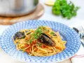 En tallrik med frutti di mare pasta, toppad med färsk persilja och serverad i en blåmönstrad skål.