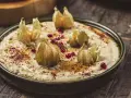 Krämig baba ganoush toppad med physalis och granatäppelkärnor på en rustik träyta.