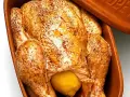 En hel kyckling med gyllene skinn och en citron i magen, redo att tillagas i en lergryta.