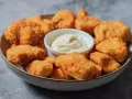 En skål med gyllene, krispiga chicken nuggets och en liten skål med krämig dipp. Perfekt för en snabb och god måltid.