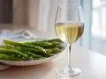 En tallrik med färsk grön sparris och ett glas vitt vin. Perfekt kombination för en lätt och god måltid.