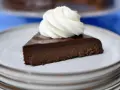 En bit krämig fransk chokladtårta med en virvel av vispad grädde på en ljusgrå tallrik.