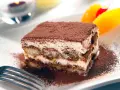 En bit krämig tiramisu, pudrad med kakao, serveras med frukt. Perfekt dryck till tiramisu.