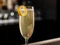 Ett glas French 75 med bubblor och citronskal. En klassisk drink med en intressant french 75 historia.