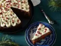 En mjuk pepparkaka med fluffig frosting och röda bär. En bit är upplagd på en blåvit tallrik, redo att avnjutas.