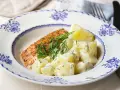 En bit lax med dill och en klyfta citron serveras med krämig stuvad potatis på en vacker blåvit tallrik.