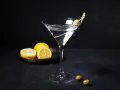 En klassisk vodka martini med en oliv på en tandpetare. Citroner ligger på en tallrik i bakgrunden.