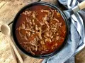 En gjutjärnspanna fylld med saftig, långkokt pulled beef i en mustig sås. Två träskedar ligger bredvid, redo att servera.