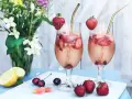 Två glas med ett uppfriskande drink med gin, fyllda med is, jordgubbar och körsbär. En perfekt sommardrink!