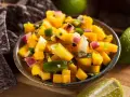 En skål med färgglad mango salsa, med tärnad mango, rödlök, grön paprika och koriander. Serveras med tortillachips och limeklyftor.