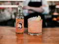 En rosa tequila drink med is och lime, bredvid en flaska Thomas Henry Pink Grapefruit.