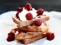 En stapel gyllene belgiska våfflor toppade med vispgrädde och färska hallon, pudrade med florsocker. En härlig frukost eller efterrätt.