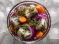 En skål med inlagd sill, rödlök, morötter och dill, serverad på is. En klassisk svensk rätt, perfekt för midsommar.