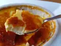 En sked tar en bit av en krämig creme brulee med karamelliserat sockerlock.