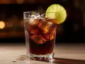 Ett glas med is och en limeklyfta, fyllt med en mörk dryck som påminner om en cuba libre.
