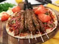 Grillade Adana kebabspett på en bädd av tunnbröd med rödlök, tomat och persilja. Ett perfekt adana kebab recept för en smakrik måltid.