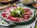 En tallrik med tunt skivad råbiff, toppad med ruccola, parmesan och kapris. Perfekt vin till carpaccio.