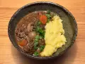 En skål med mustig biff bourguignon med möra köttbitar, champinjoner, lök och morötter, serverad med krämigt potatismos och garnerad med persilja.